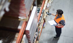 Pick and pack warehouse worker in a high vis vest scans a product on a shelf holding a clipboard
