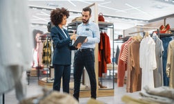 Two retail store staff members standing in between clothing racks looking at iPad.