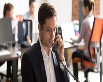 hard of hearing man holding desk phone land line in an office setting