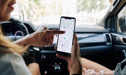 Woman holding smartphone showing vehicle tracking via gps of vehicles in the local area to other person in car