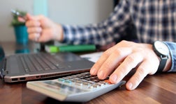 business person calculating payroll details using calculator and laptop with pen in hand
