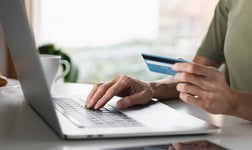 Woman using laptop holding credit card making online payment.