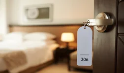 Open hotel room door with room 206 key in door on foreground and double bed and side table out of focus in background