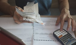 person calculating debt using receipts, bills and other documents on a table beside a calculator