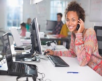 Smiling female employee talking on cordless phone while sitting at desk.