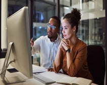 Two professionals collaborating on a project in the office at night