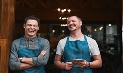Smiling restaurant workers standing in doorway holding tablet.