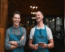 Smiling restaurant workers standing in doorway holding tablet.