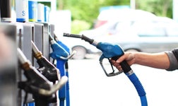 A person's hand holding a blue fuel pump nozzle at a gas station.
