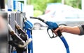 A person's hand holding a blue fuel pump nozzle at a gas station.