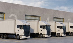 trucks lined up by angled to the left in a delivery depot waiting to be filled with goods on a sunny day with a few clouds in the sky
