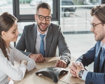 Three business people sitting at desk talking on conference phone.