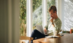 Man sitting on sofa in home smiling while looking at laptop.