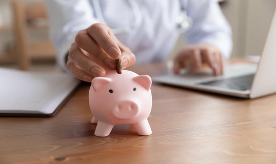 Person putting coin into piggy bank while using a laptop