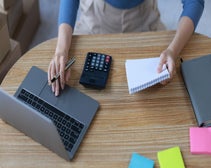 Person working on laptop and a notepad to work out how to get a merchant account for their business