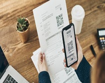 person holding invoice and scanning a QR code using smartphone with other hand