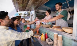 Smiling food truck workers handing drinks to customers.