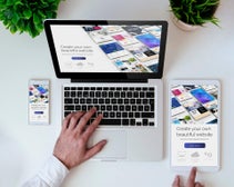 A laptop and smartphone displaying a responsive website design interface on a white desk, surrounded by green plants.
