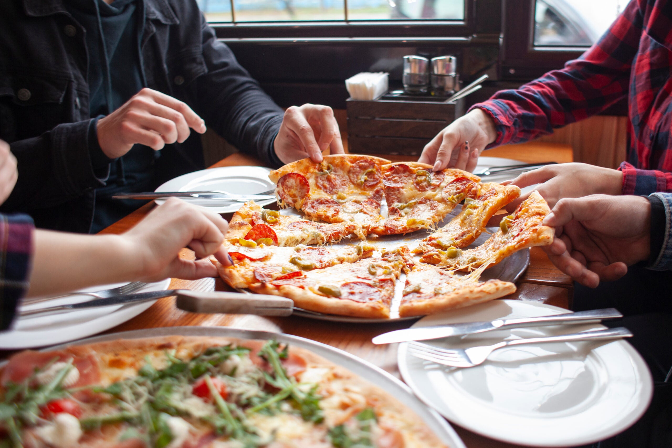 Gros plan sur les mains d'un groupe d'amis en train de se servir des parts de pizza.