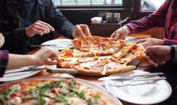 Gros plan sur les mains d'un groupe d'amis en train de se servir des parts de pizza.