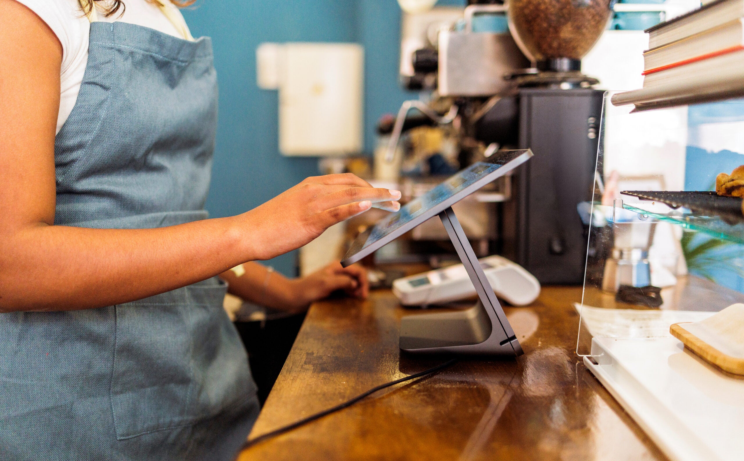 Une barista qui utilise une caisse enregistreuse format tablette sur le comptoir d'un café moderne.