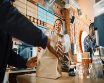 Fast food worker hands order in a paper bag over the counter to a food delivery courier.