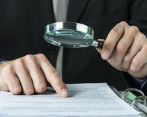A close-up image showing a person examining a document with a magnifying glass