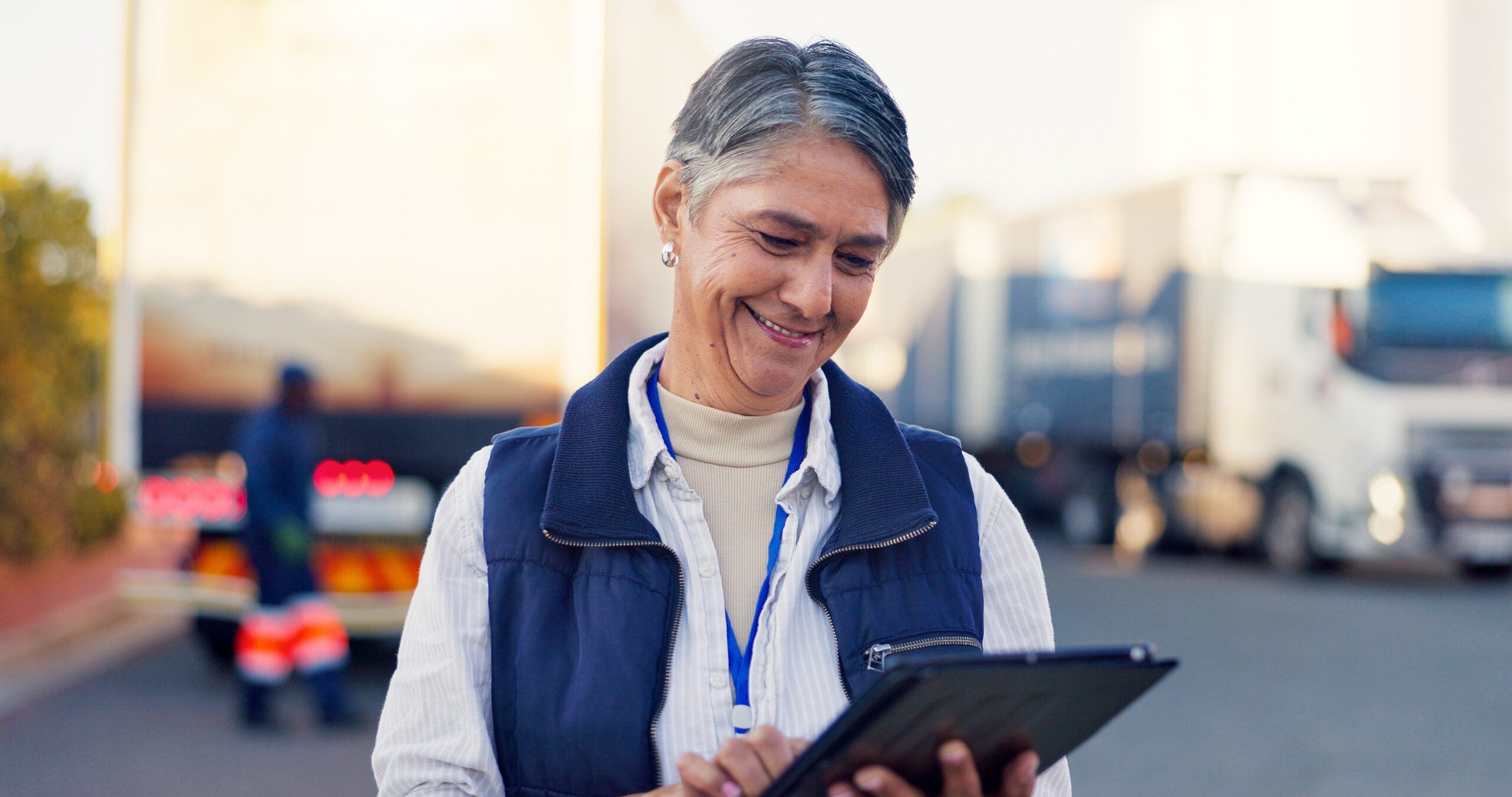 Dame professionelle souriante tenant une tablette devant des camions.
