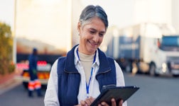 Dame professionelle souriante tenant une tablette devant des camions.