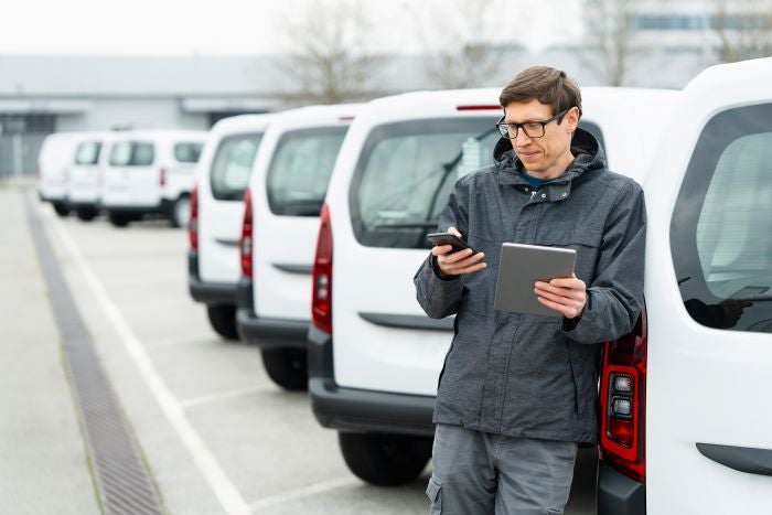 Un chef de flotte devant des camions avec un fichier et téléphone