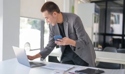 man standing over laptop with phone in hand
