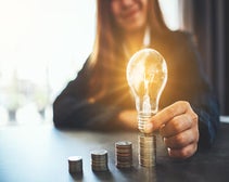 Woman placing lightbulb on top of coins