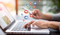 Hands typing on a laptop keyboard with floating social media interaction icons, depicting active engagement on social media platforms.