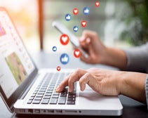 Hands typing on a laptop keyboard with floating social media interaction icons, depicting active engagement on social media platforms.