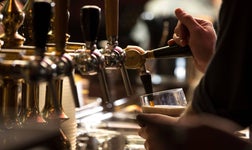Close up of bartender filling a glass with beer from a tap in dimly lit pub.