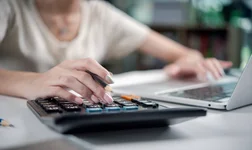 Businesswoman at desk using a calculator and laptop