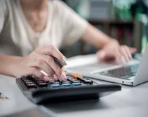 Businesswoman at desk using a calculator and laptop