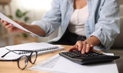 Close-up of a person calculating budget with a calculator and reviewing financial documents on a desk.