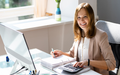 woman accountant using a calculator while sitting at a desk in front of a computer