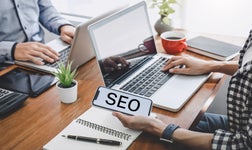 two office workers on laptops, phone screen displays 