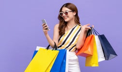 Woman wearing sunglasses holding shopping bags smiling at phone