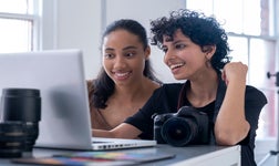 two women using a computer with a camera in front of them