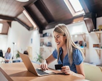 Smiling young woman completing online purchase on laptop while holding credit card