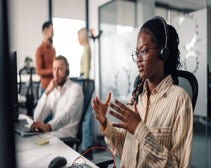 person on the phone using a headset for VoIP calling in a dynamic office setting, three people behind blurry