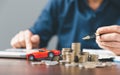 Using a calculator next to a pile of coins and a red toy car