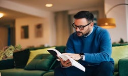 man reading book while sat on a sofa