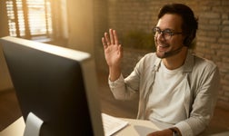 man waving at pc while on VoIP call