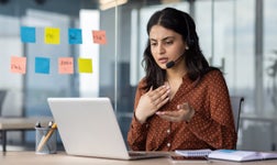 woman on phone with headset in an office talking to laptop screen