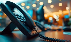 A VoIP-compatible desk phone sitting on a stand in an office.