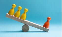 Close-up Of Red And Yellow Pawns Figures Balancing On Wooden Seesaw Over Blue Surface
